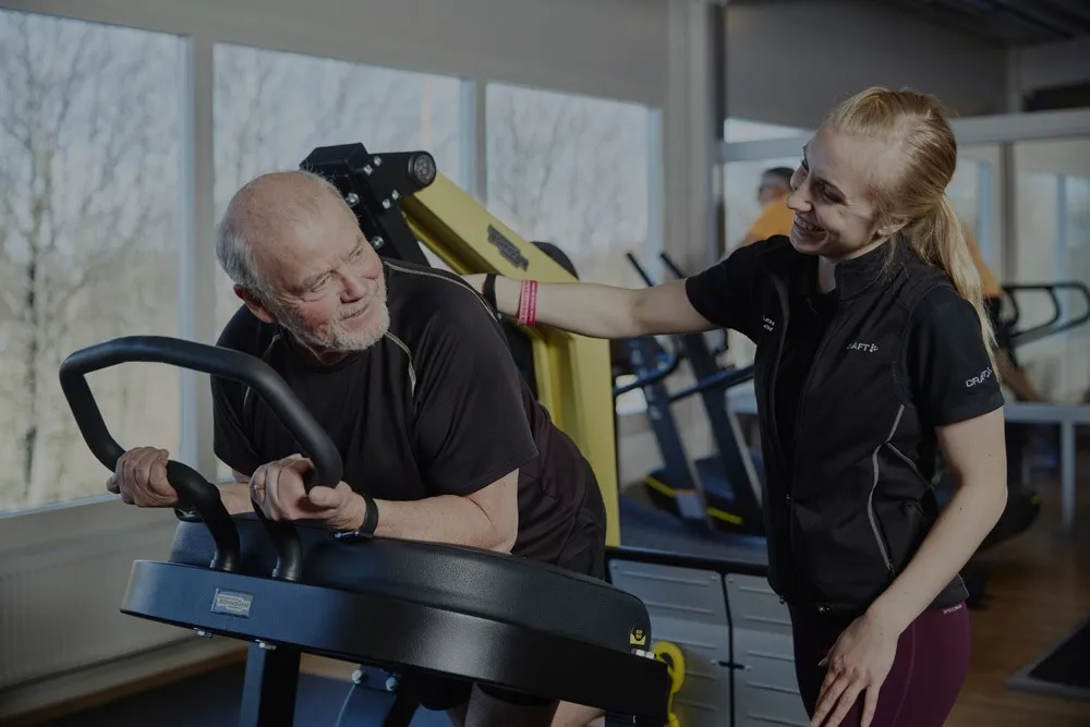 yngre människa hjälper en senior att träna med maskin på gym