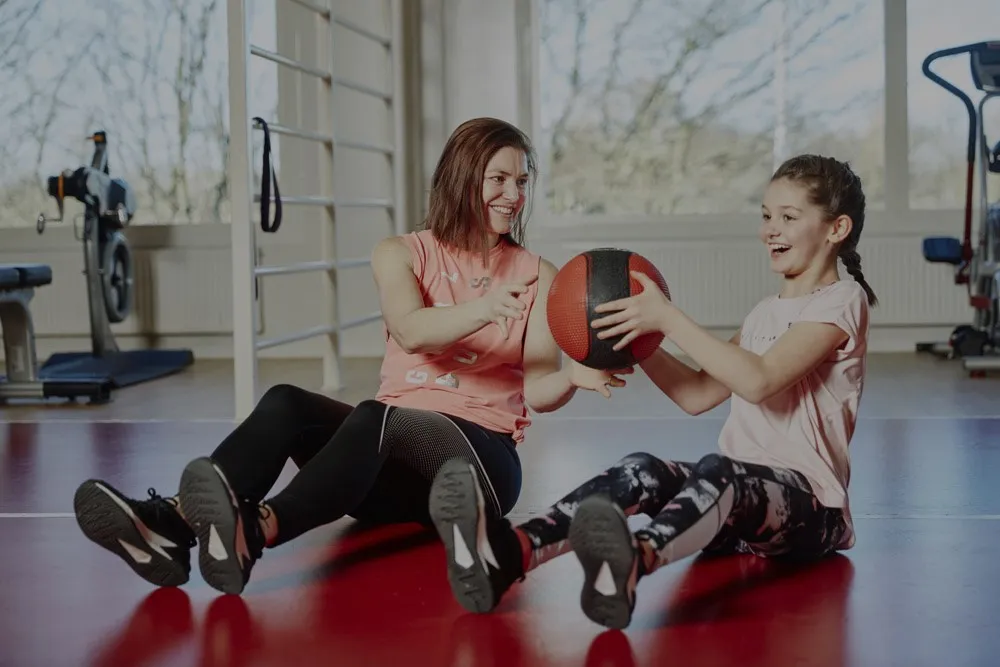Kvinna och barn skickar en medicinboll mellan sig i ett gym